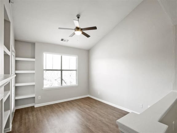 an empty living room with a ceiling fan and a window