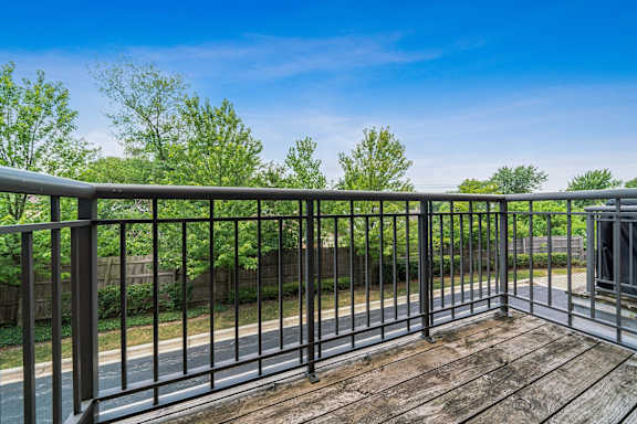 A wooden deck with a metal railing overlooks a road and greenery.