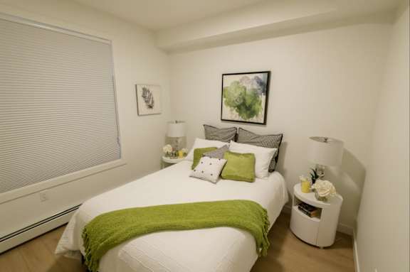 A white bedroom with a bed, nightstand, and lamp.