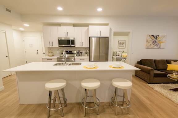 A modern kitchen with white cabinets and a white island with two stools.