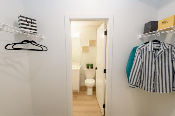 A white bathroom with a toilet and a striped shirt hanging on the wall.