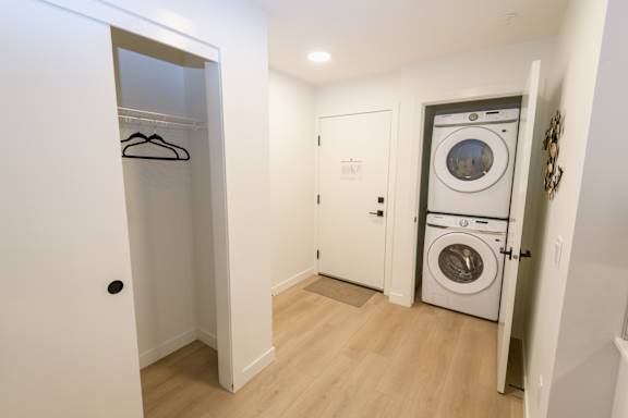 A white door with a black handle is open to a hallway with a washer and dryer in the other room.