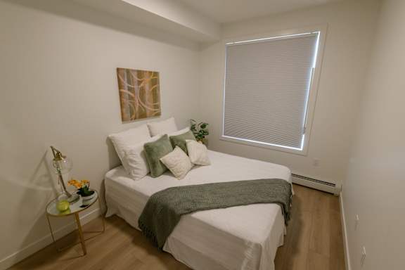 A bedroom with a bed, pillows, a blanket, a nightstand, and a painting on the wall.