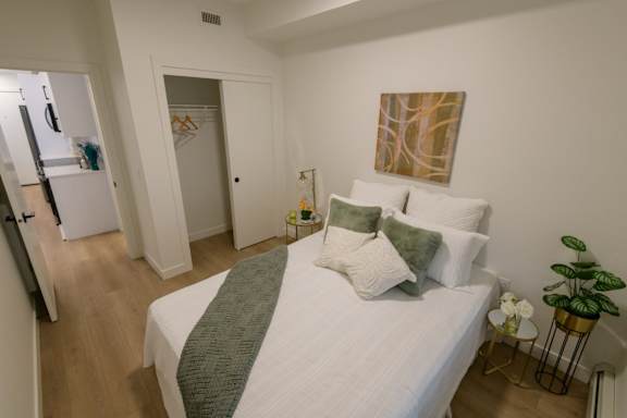 A bedroom with a bed, nightstand, and a plant.