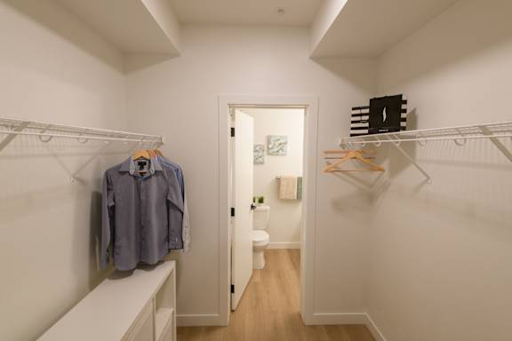 A white hallway with clothes hanging on a rack and a toilet in the background.