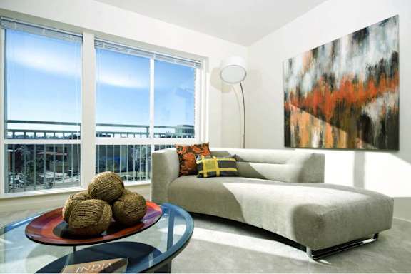 A modern living room with a grey couch, a glass table, and a large painting on the wall.