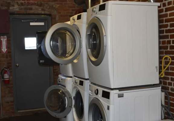 A stack of white washing machines in front of a brick wall.