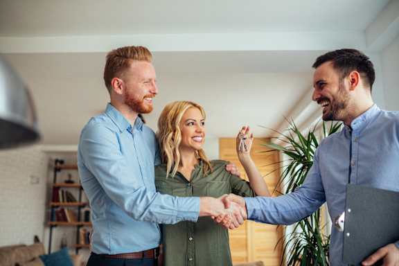 Two men shake hands with a woman in a room.
