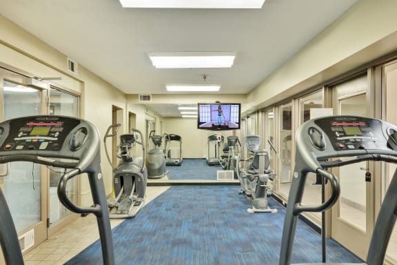 a gym with cardio machines and a tv