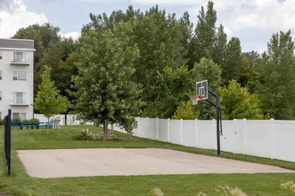 a basketball hoop on the grass in front of a white fence
