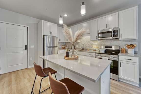 A kitchen with white cabinets and a white island with two chairs at Lochner Apartments, White Bear Lake, 55110