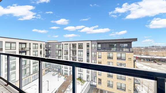 A modern apartment complex with a glass balcony overlooking a snowy parking lot.