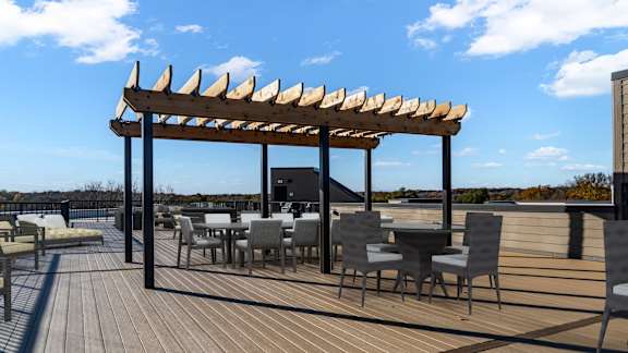 A wooden deck with tables and chairs under a pergola.