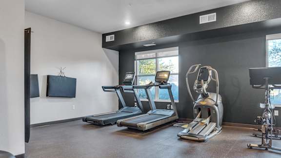 A gym room with treadmills, exercise bikes, and a television.