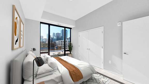 A bedroom with a large bed and a city view through the window.