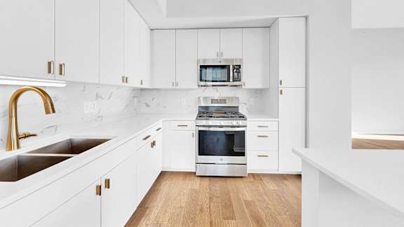 A modern kitchen with white cabinets and a wooden floor.