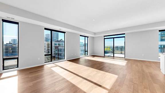 A spacious room with wooden floors and large windows overlooking the city.