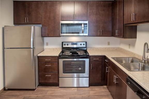 A kitchen with a stainless steel refrigerator, a stainless steel oven, and brown cabinets.