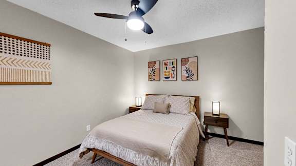 A bedroom with a bed, nightstand, and a ceiling fan.