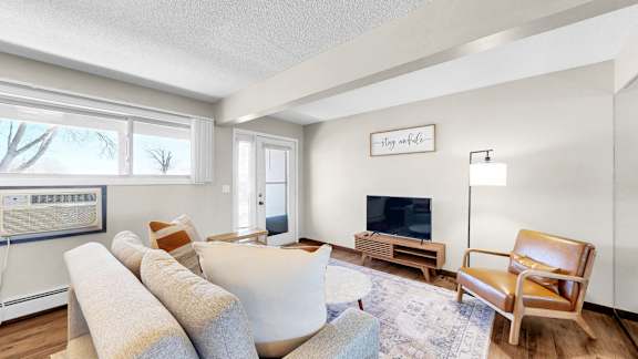 A living room with a white couch, a wooden chair, and a television on a stand.