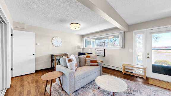 A living room with a grey couch, a wooden table, and a white wall clock.