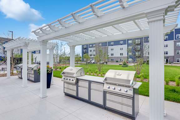 A white pergola is over a grill and table at Lochner Apartments, White Bear Lake