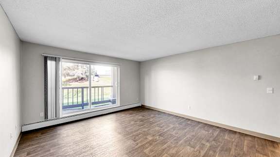A room with wooden flooring and a sliding glass door leading to a balcony.