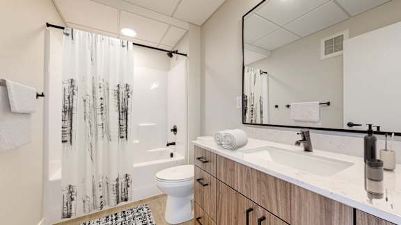 A bathroom with a white toilet, a sink, and a shower curtain with black and white trees on it.