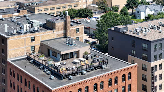 A rooftop patio with a bar and chairs is surrounded by buildings.