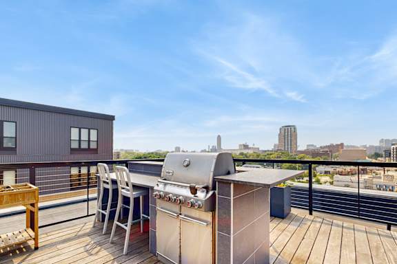 A grill is on a wooden deck with a table and chairs.