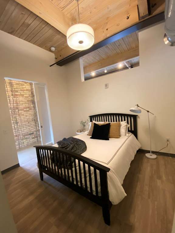 A bedroom with a bed, wooden headboard, and a white bedspread.