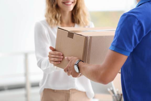 A delivery person is handing a cardboard box to a woman.