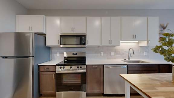 A modern kitchen with stainless steel appliances and wooden cabinets at Ardor on the Bluffs South Loop Residences Apartments, Bloomington