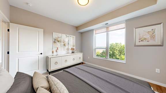 A bedroom with a large bed and a dresser with a mirror at Ardor on the Bluffs South Loop Residences Apartments, Bloomington, Minnesota