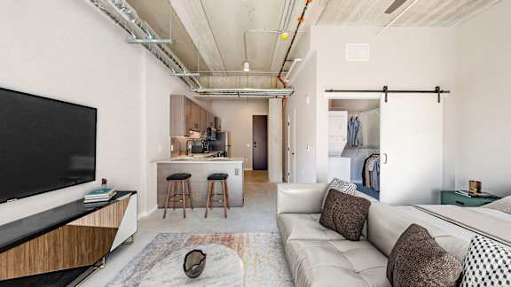 A modern living room with a white couch and a television on the left side at Ardor on the Bluffs South Loop Residences Apartments, Bloomington, MN