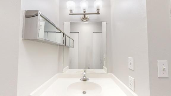 A white sink in a bathroom with a mirror and lights above it.