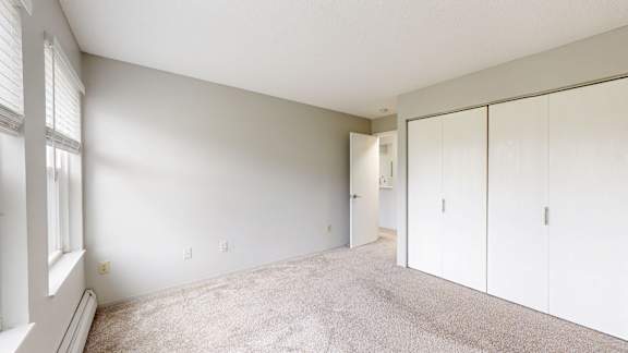 A room with white walls and carpeted floor with a window on the left.
