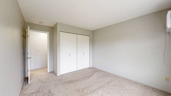 A room with white walls and carpeted floor with a white door and two white closet doors.