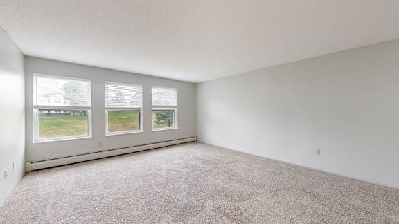 A room with a carpeted floor and a large window with a view of a house and trees outside.