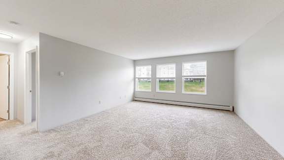 A room with a carpeted floor and a window with a view of a green lawn.