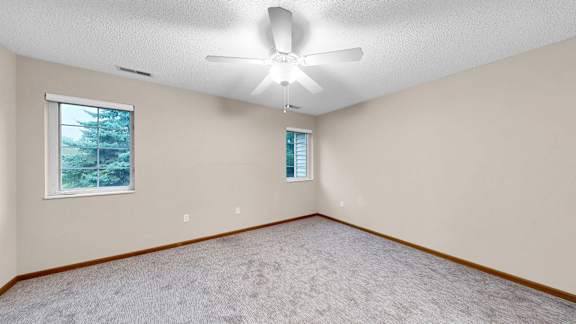 A room with a ceiling fan and two windows.