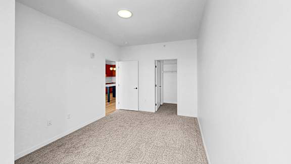 A room with white walls and carpeted floor with a door on the right.