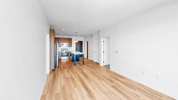 A long, empty hallway with a blue chair and a kitchen in the distance.