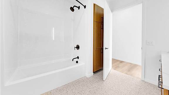 A white bathroom with a wooden door and a tiled floor.