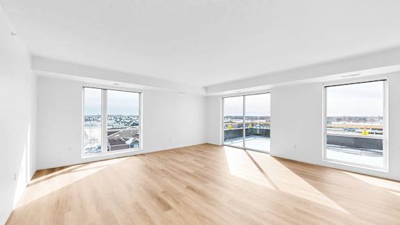 A large empty room with wooden floors and windows overlooking a cityscape.