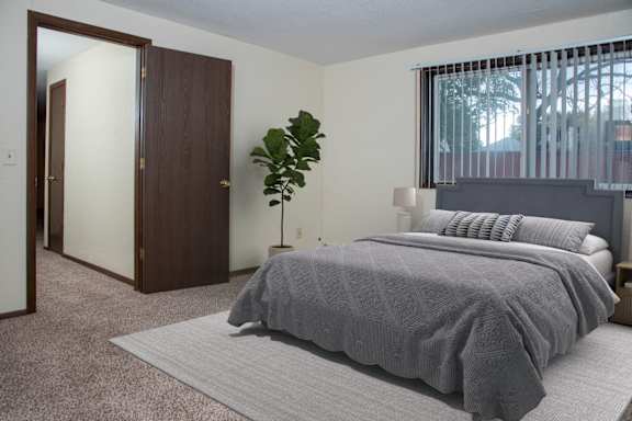 A bedroom with a bed, a plant, and a window.
