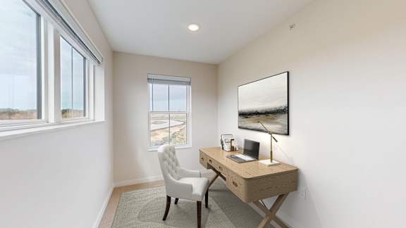 A room with a desk and chair with a window and a painting on the wall.