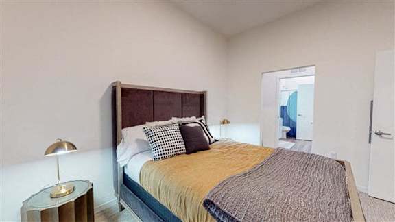 A bedroom with a bed, nightstand, and lamp at The Bessemer at Seward Commons Apartments, Minnesota