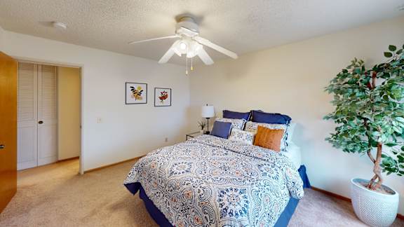 A bedroom with a bed, a ceiling fan, and a potted plant.