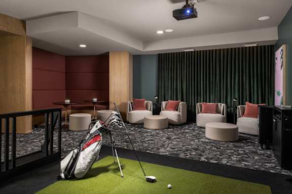 A golf club is propped up against a wall in a room with a green carpet.